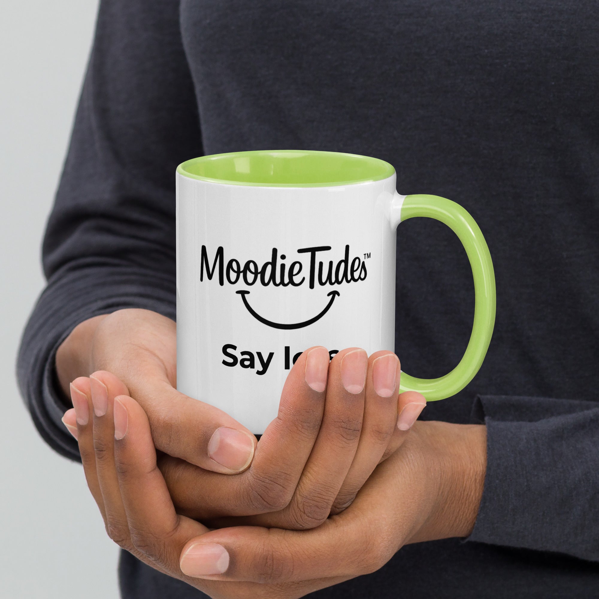 MoodieTudes™ Say Less mug, hand held with logo and tag line visible